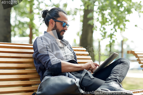 Image of man with tablet pc sitting on city street bench