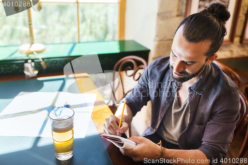 Image of man with beer writing to notebook at bar or pub