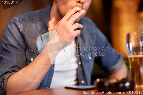 Image of man drinking beer and smoking cigarette at bar