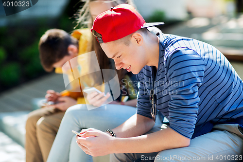 Image of happy teenage friends with smartphones outdoors