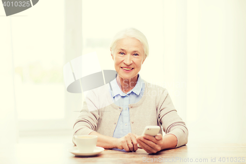 Image of senior woman with smartphone texting at home