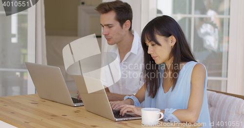 Image of Calm young couple sitting at table using laptop