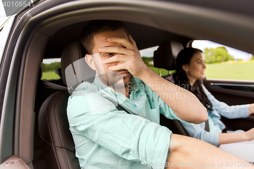 Image of woman driving car and man covering face with palm