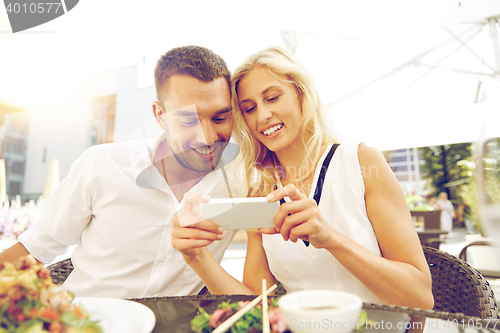 Image of happy couple with smatphone at restaurant terrace