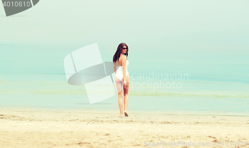 Image of young woman in swimsuit walking on beach