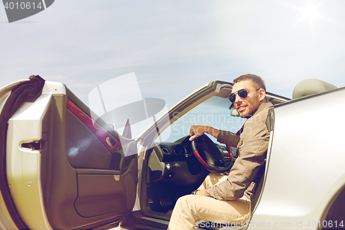 Image of happy man opening door of cabriolet car outdoors