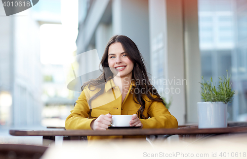 Image of happy woman drinking cocoa at city street cafe