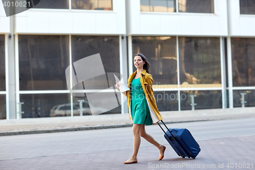 Image of happy young woman with travel bag and map in city