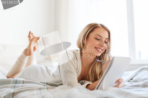 Image of happy young woman with notebook in bed at home