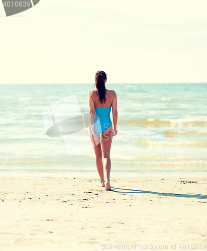 Image of young woman in swimsuit walking on beach