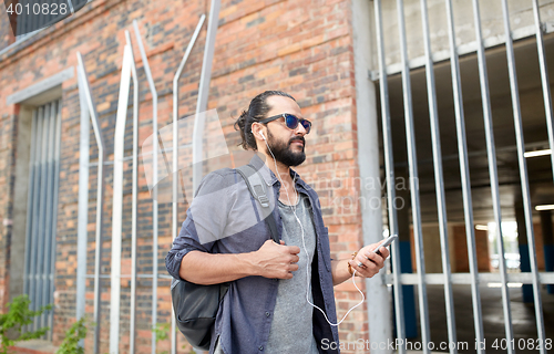 Image of man with earphones and smartphone walking in city