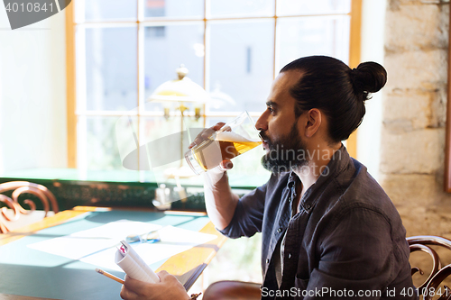 Image of man with notebook drinking beer at bar or pub