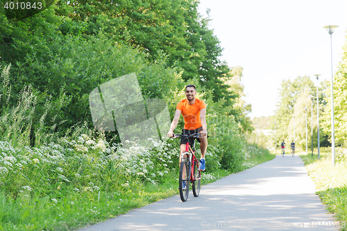 Image of happy young man riding bicycle outdoors