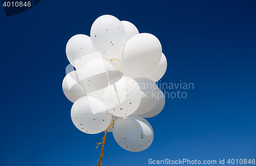 Image of close up of white helium balloons in blue sky