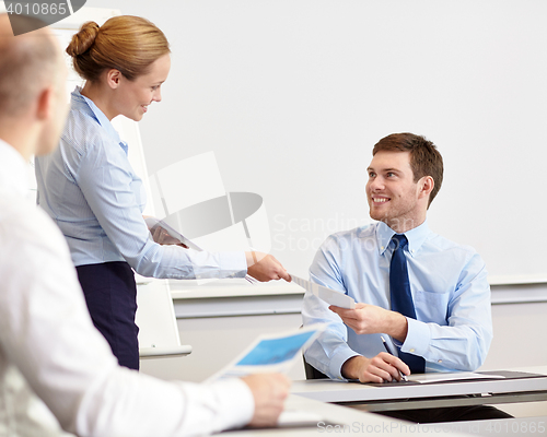 Image of smiling woman giving papers to man in office