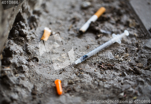 Image of close up of syringe and smoked cigarette on ground