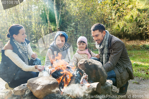 Image of happy family roasting marshmallow over campfire