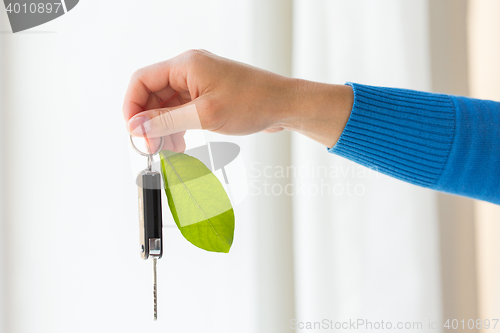 Image of close up of hand holding car key with green leaf