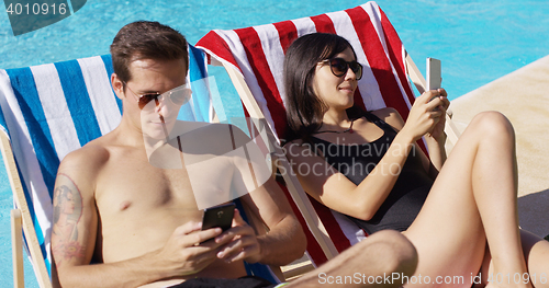 Image of Young couple using phones at the swimming pool
