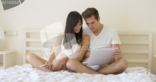 Image of Couple sitting together in bed using computer