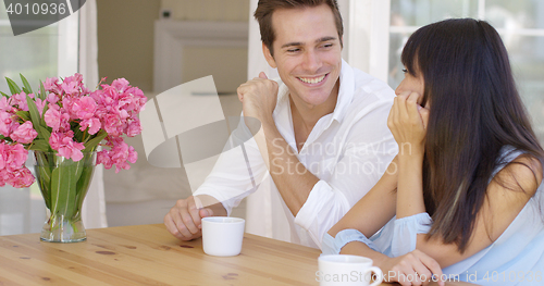 Image of Joyful mixed adult couple sitting at table