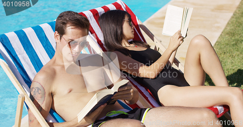 Image of Relaxed attractive young couple reading poolside