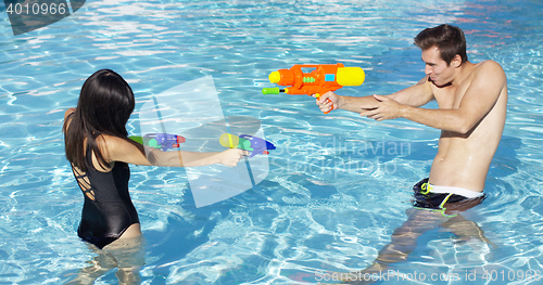 Image of Happy couple shooting off water guns in pool