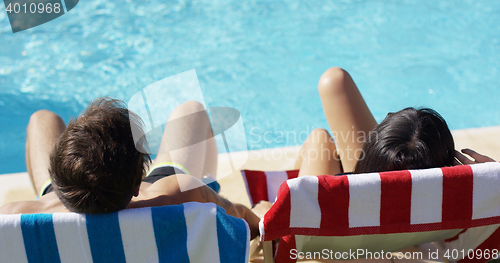 Image of Couple relaxing in colorful deck chairs poolside