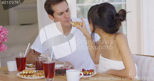 Image of Woman trying to feed annoyed man a waffle