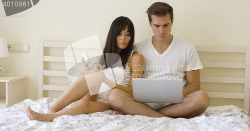 Image of Young serious couple sitting together in bed