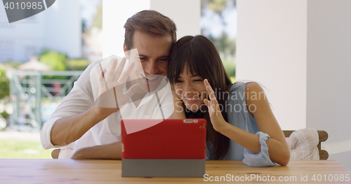 Image of Man and woman waving at their tablet computer