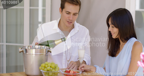 Image of Smiling young couple pouring champagne to drink
