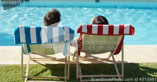 Image of Couple relaxing in colorful deck chairs poolside