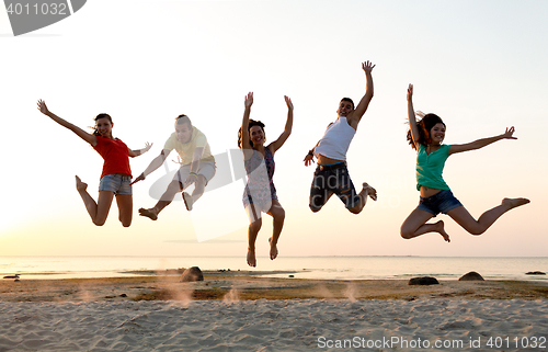 Image of smiling friends dancing and jumping on beach