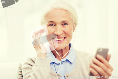 Image of senior woman with smartphone and earphones at home