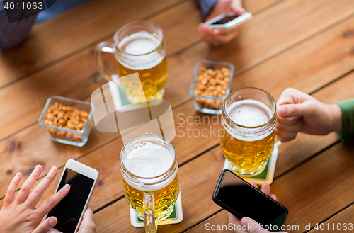 Image of close up of hands with smartphones and beer at bar