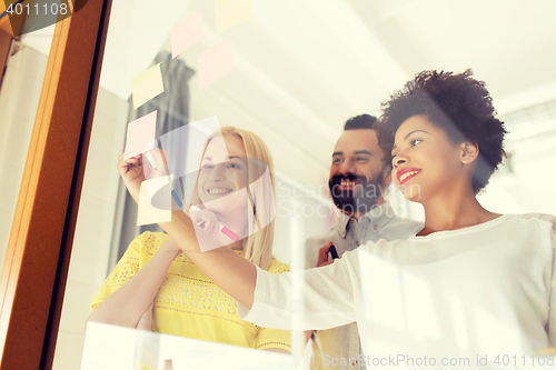 Image of happy creative team writing on stickers at office