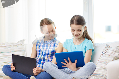 Image of happy girls with tablet pc sitting on sofa at home