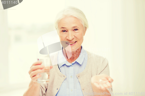 Image of happy senior woman with water and medicine at home