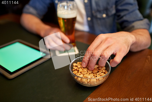 Image of man with tablet pc, beer and peanuts at bar or pub