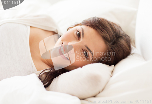 Image of smiling young woman lying in bed at home
