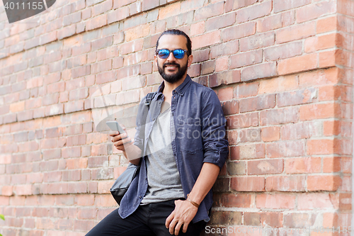 Image of man with backpack texting on smartphone in city