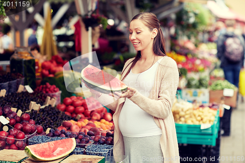 Image of pregnant woman holding watermelon at street market