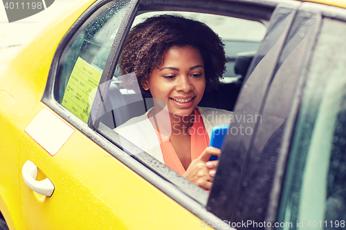 Image of happy african woman texing on smartphone in taxi