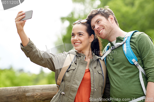 Image of couple with backpacks taking selfie by smartphone