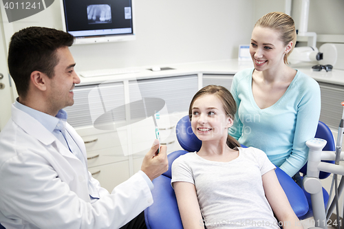Image of happy dentist showing toothbrush to patient girl