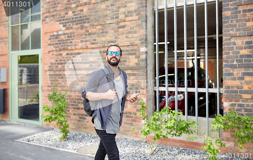 Image of man with earphones and smartphone walking in city