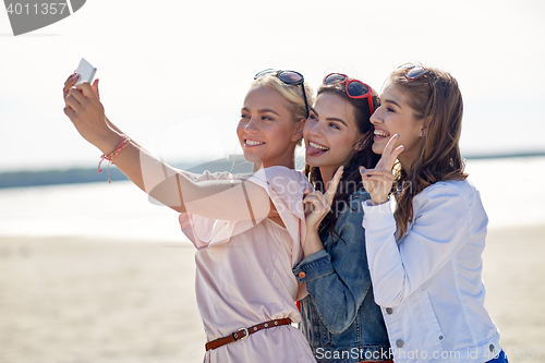 Image of group of smiling women taking selfie on beach