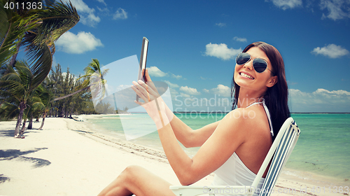 Image of smiling woman with tablet pc sunbathing on beach