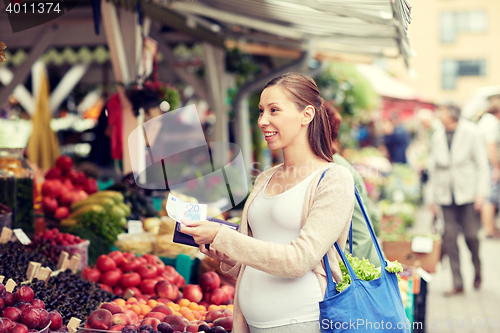 Image of pregnant woman with wallet buying food at market